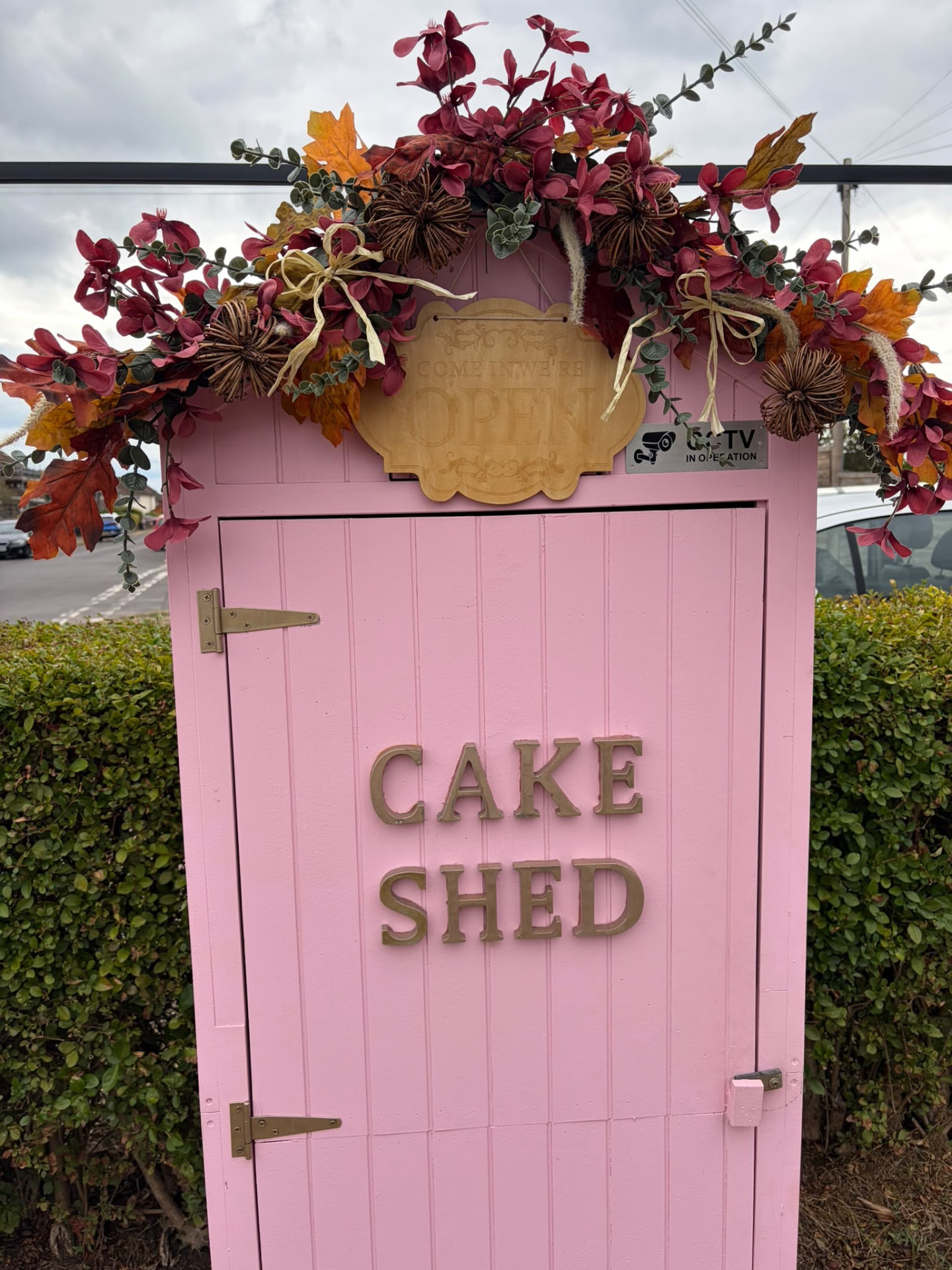 Pink Cake Shed in Egham decorated with autumn flowers and a 'come in we're open' sign