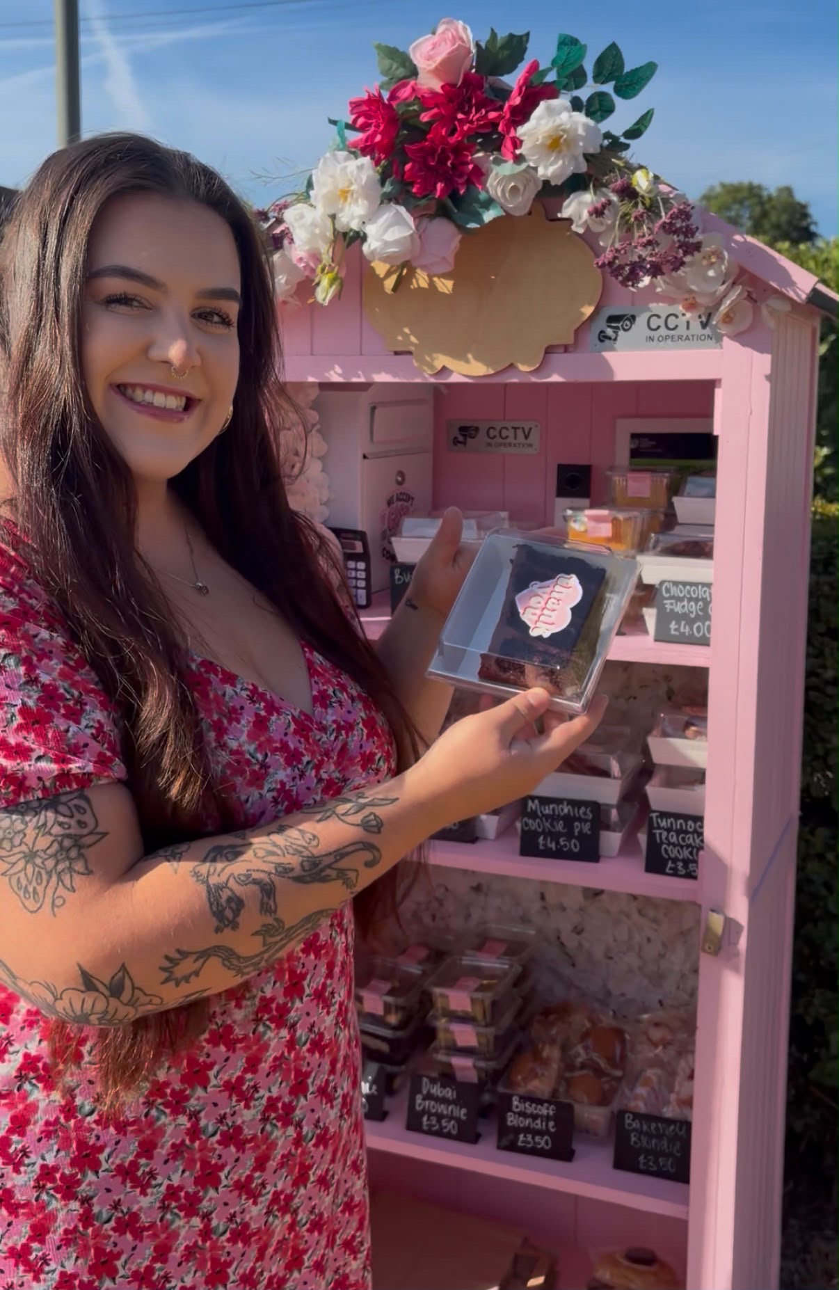 Billie holding a boxed brownie in front of the fully stocked pink Cake Shed in Egham
